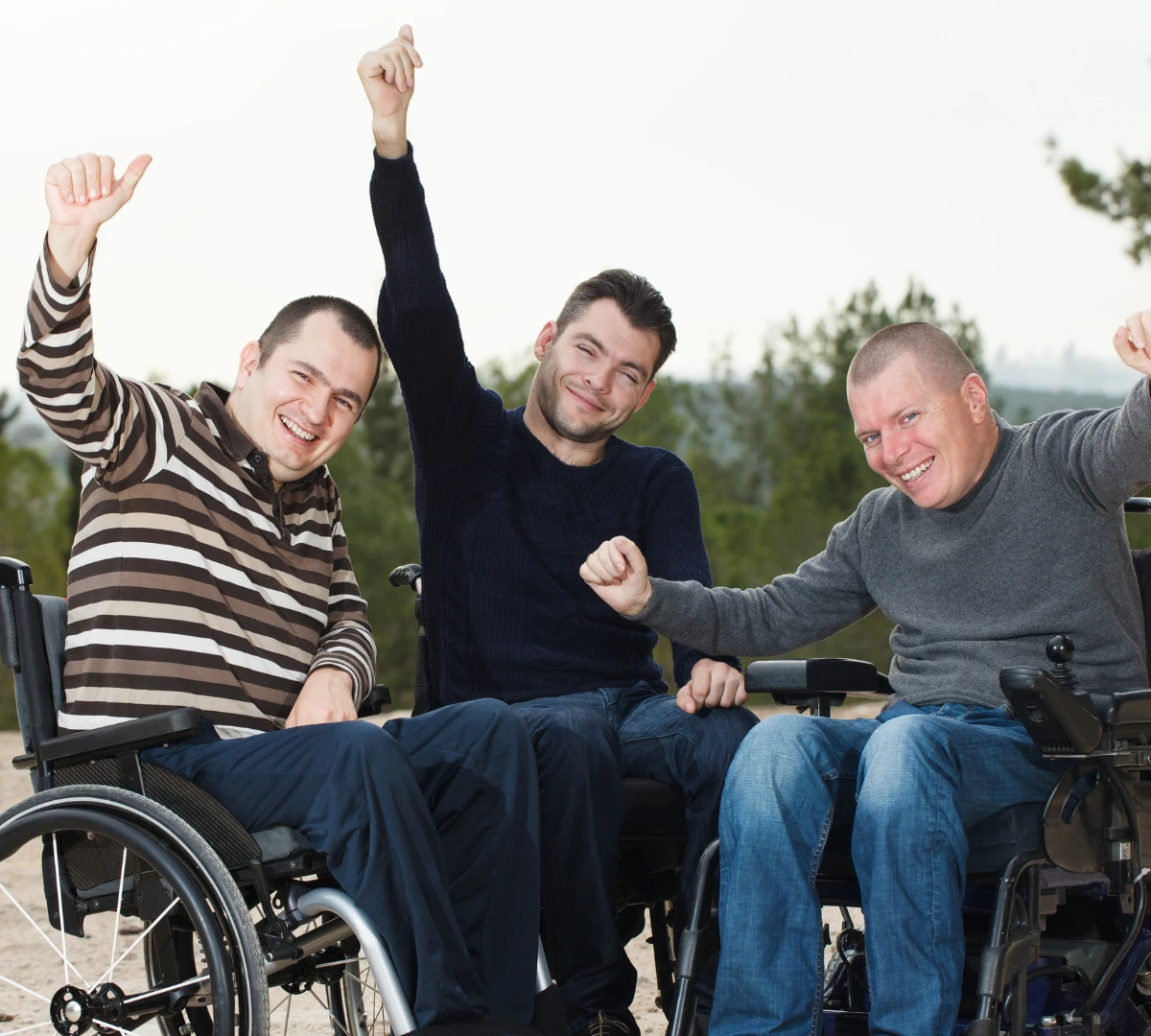 Three disabled friends in wheelchairs smiling with hands in the air