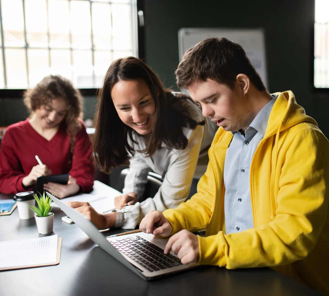 Disabled man with down syndrome using laptop with support worker