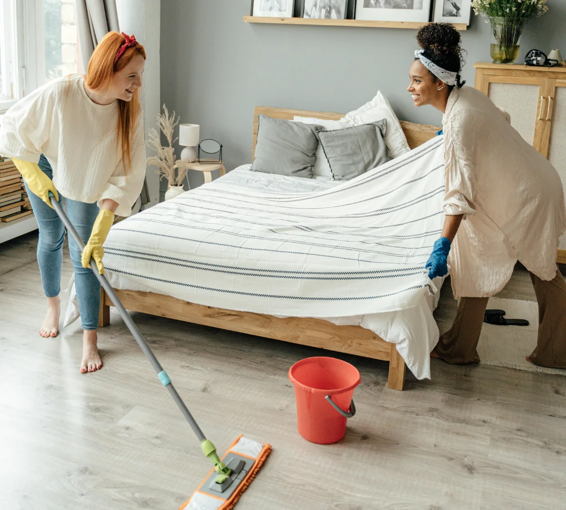 Two support workers making bed and mopping floor