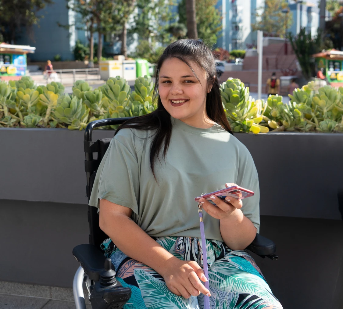 Disabled woman in wheelchair holding phone and looking at camera smiling